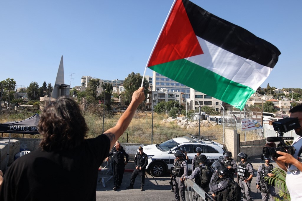 Un militant brandit un drapeau palestinien à l’entrée de Sheikh Jarrah, à Jérusalem-Est, le 25 juin 2021 (AFP)