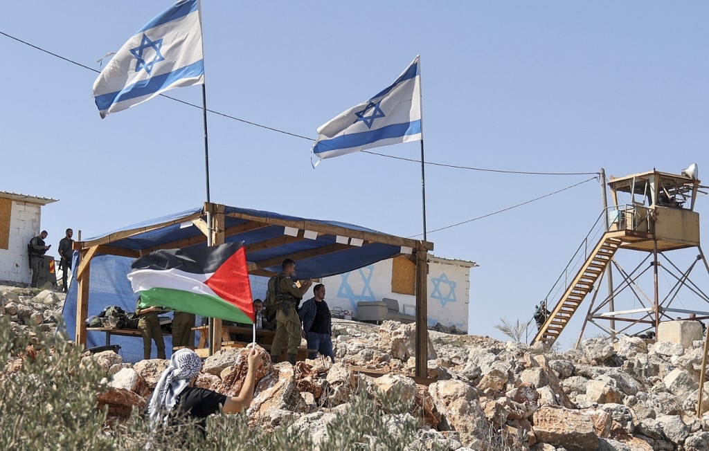 A Palestinian man waves his country's flag next to the Israeli settlement outpost of Evitar in the village of Beita, north of Nablus in the occupied West Bank, on 10 October 2021 (AFP)
