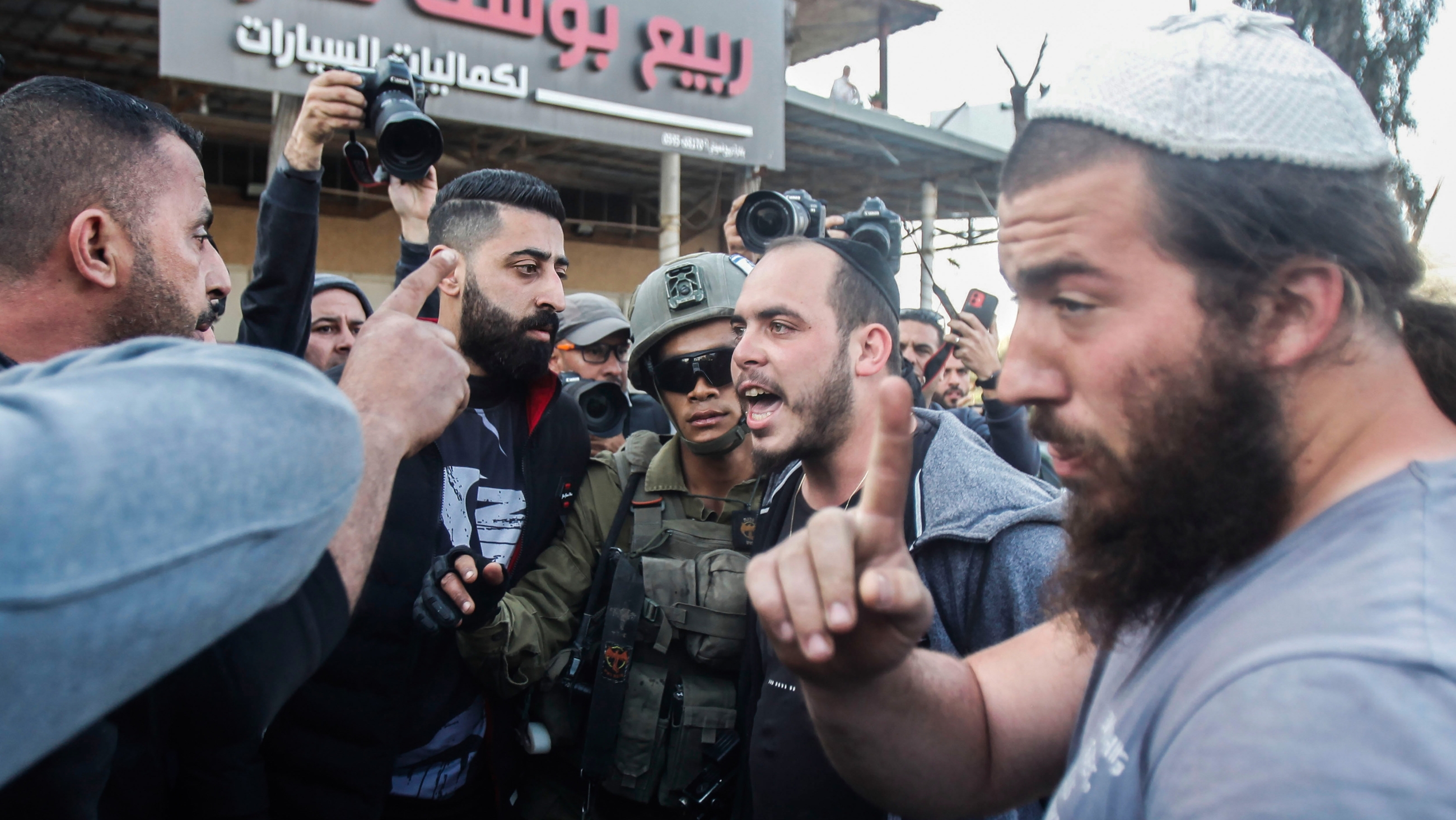 Israeli settlers confront Palestinians while soldiers stand in between them in the occupied West Bank town of Huwwara on 27 February 2023 (Reuters)