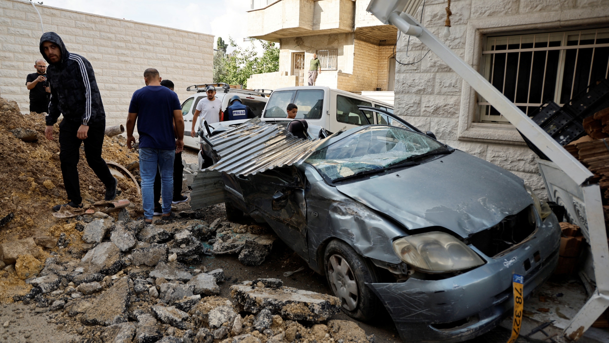 People stand next to a damaged vehicle following an Israeli military raid, at Tulkarm camp, in the Israeli-occupied West Bank 14 November 2023 (Reuters)