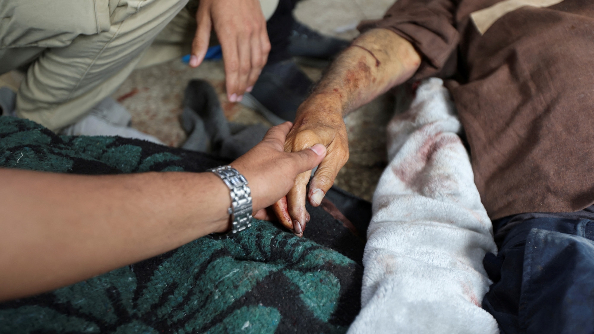 A mourner holds the hand of a Palestinian killed in Israeli strikes at Al-Aqsa hospital in Deir al-Balah in the central Gaza Strip 12 May 2024 (Reuters/Ramadan Abed)