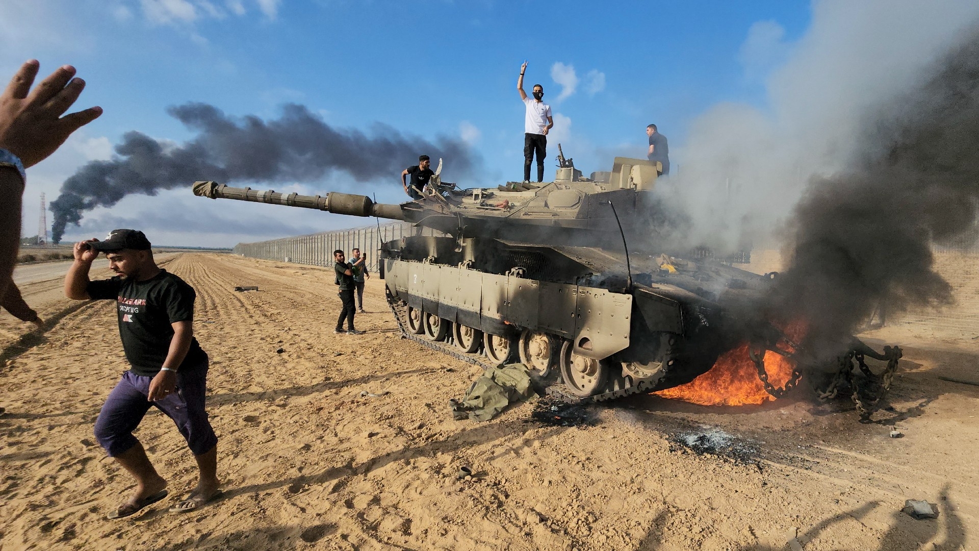 Palestinians celebrate by a destroyed Israeli tank at the Gaza Strip fence east of Khan Younis (AP)
