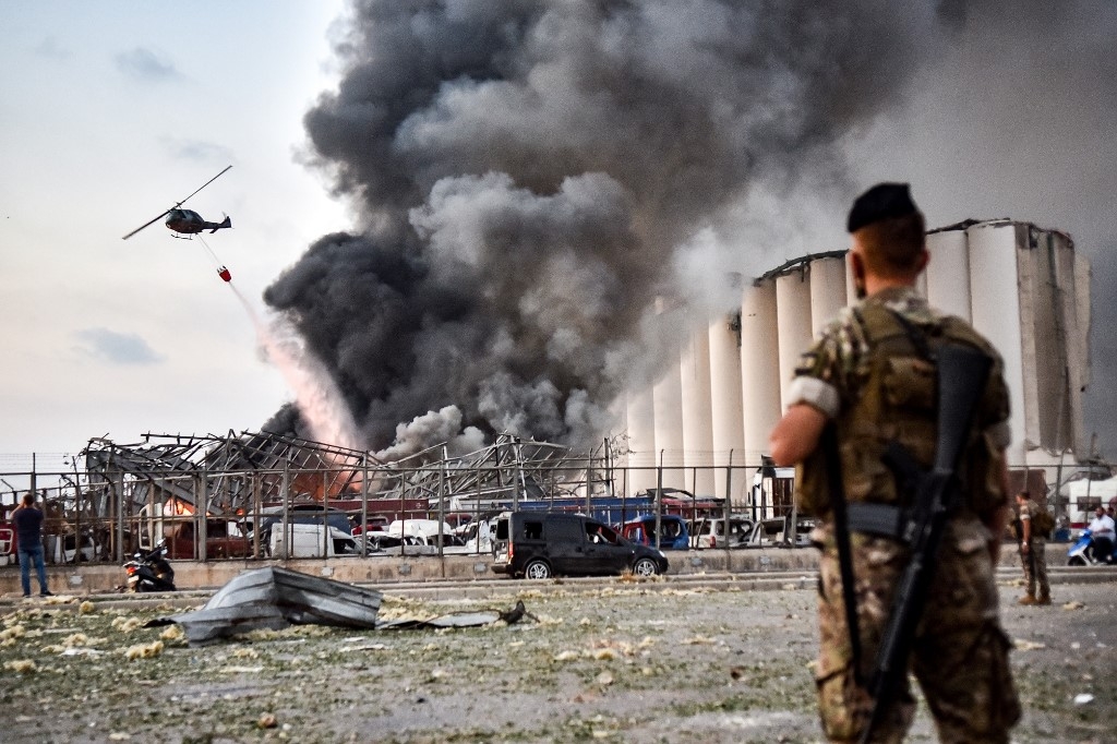 Lebanese soldiers stand guard while a helicopter puts out a fire at the scene of the explosion