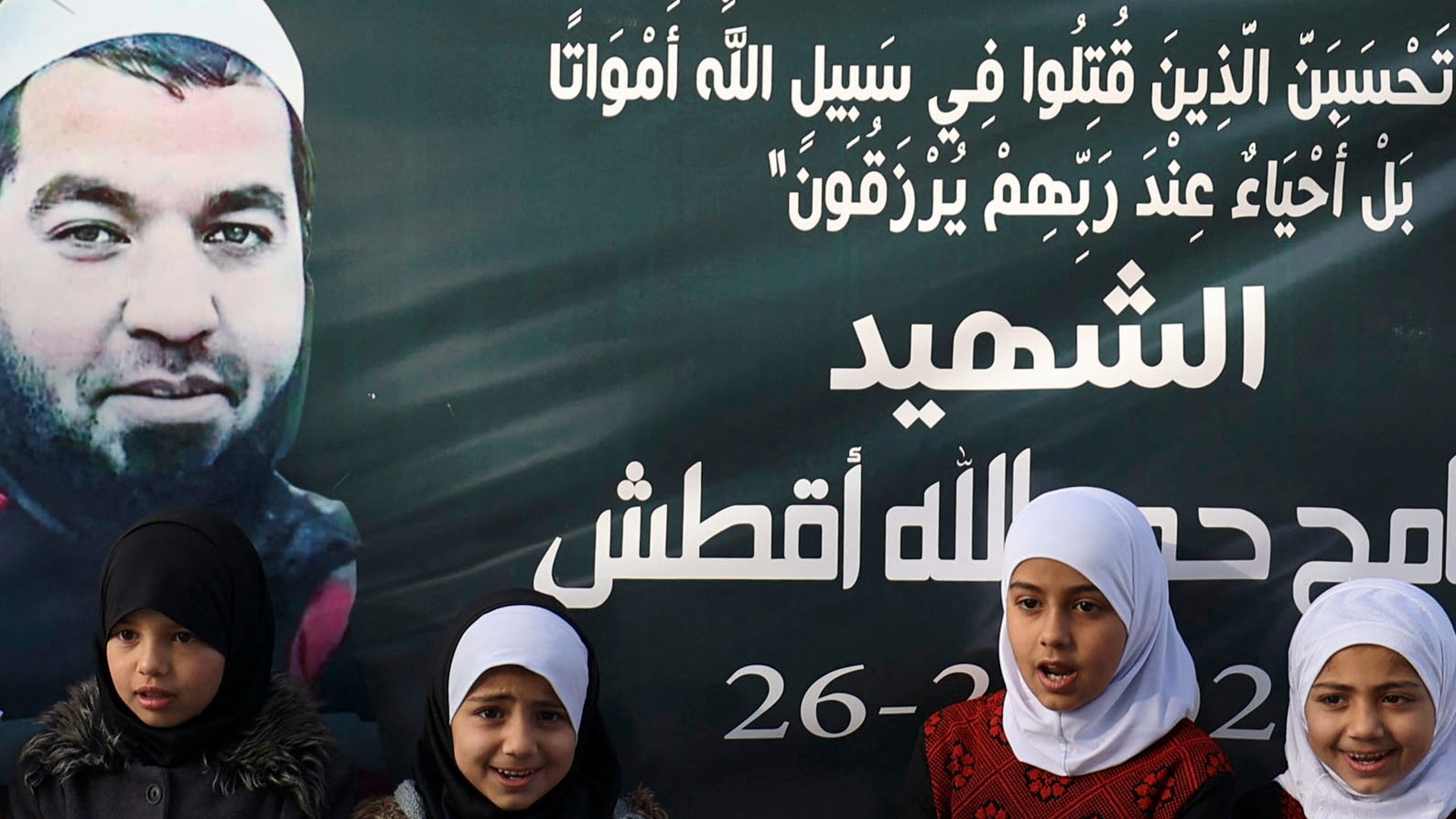Children sit under a banner displaying a picture of Palestinian Sameh al-Aqtash, 37, who was shot dead during an attack by Israeli settlers (AFP)