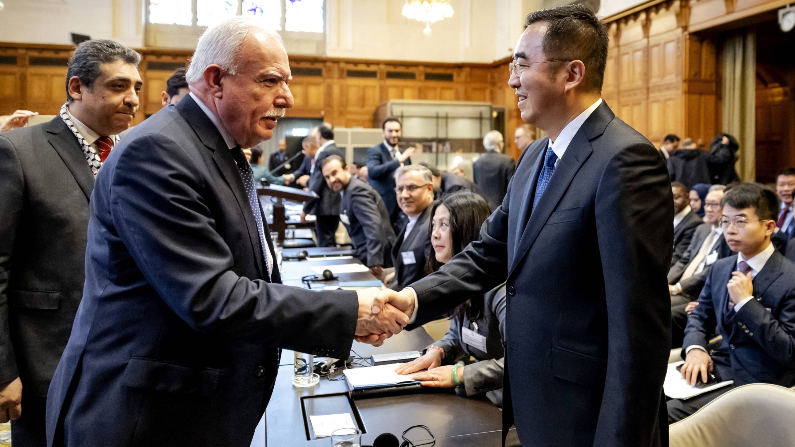 Palestinian Foreign Minister Riyad Al-Maliki (L) shakes hands with Ma Xinmin (R), China's foreign ministry legal advisor, during a hearing at the International Court of Justice in The Hague, 22 February 2024 (AFP)