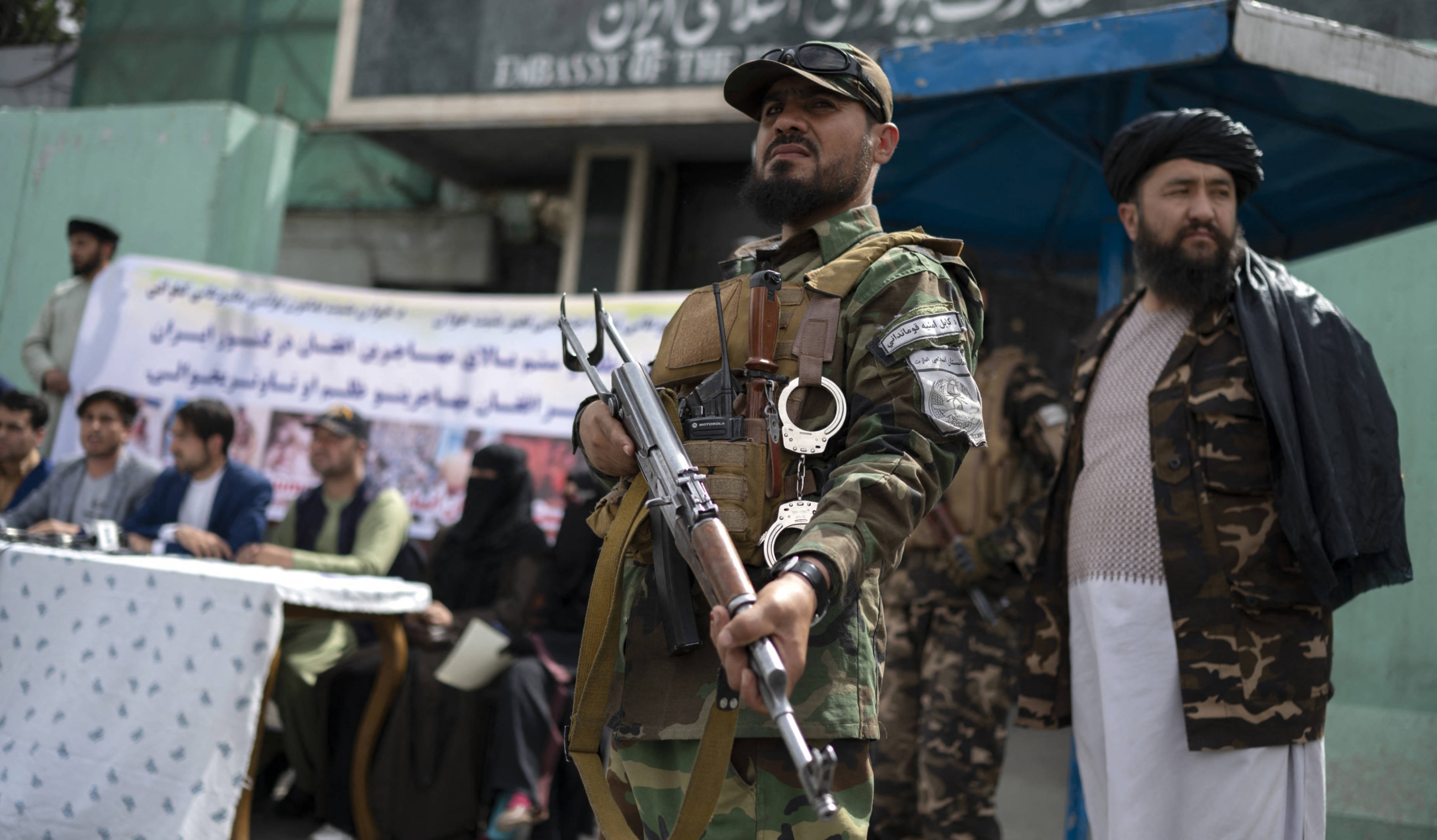 Taliban fighters stand guard as Afghan protesters take part in a demonstration against reports of harassment of Afghan refugees in Iran, in front of the Iranian embassy in Kabul on 11 April 2022