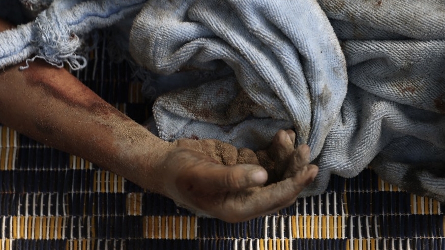 The hand of a dead Palestinian pokes out from under a blanket following an Israeli air strike on buildings in Rafah, in the southern Gaza Strip, on 17 October 2023 (AFP)