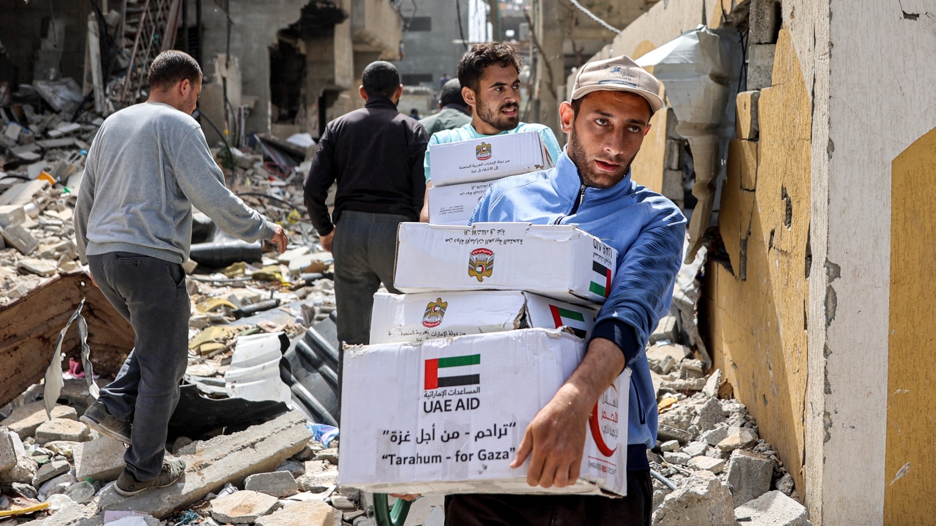 Men walk through rubble past damaged buildings with humanitarian aid packages collected from a drop over the northern Gaza Strip on 23 April 2024 (AFP)