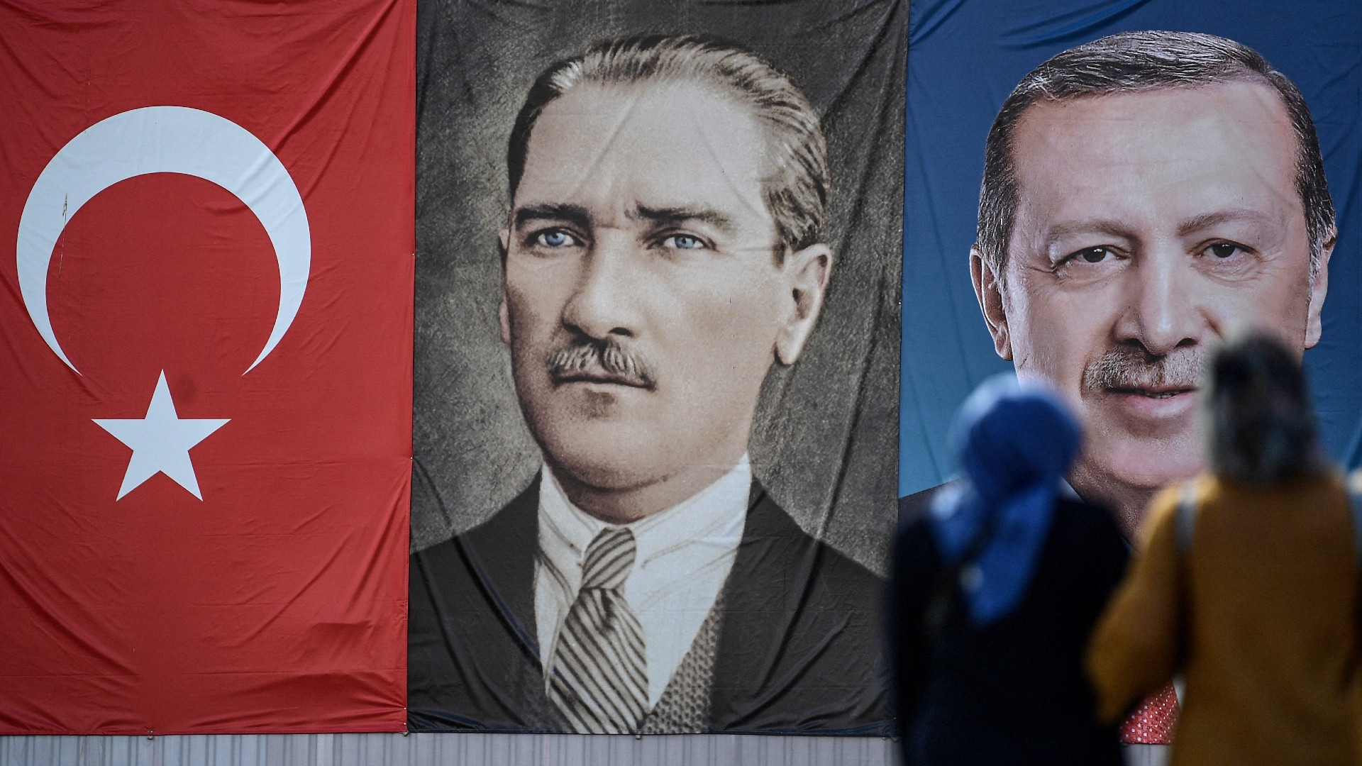 Two women stand in front of the portraits of Turkish President Recep Tayyip Erdogan, right, and founder of modern Turkey Mustafa Kemal Ataturk, left, at Emininonu district in Istanbul on 11 May 2018 (Ozan Kose/AFP)
