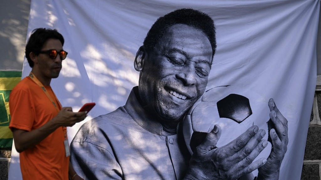 A mourner passes by a piece of cloth with an image of Brazilian football legend Pele outside the Urbano Caldeira stadium in Santos, Sao Paulo State, Brazil, on 2 January 2023 (AFP)