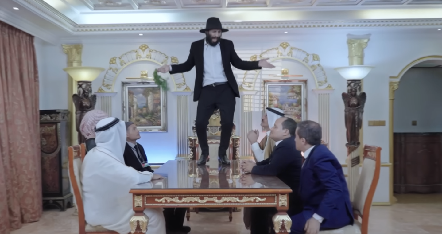 Alors que Mustafa al-Momri danse sur la table, les dirigeants arabes humiliés le regardent en souriant et l’applaudissent (capture d’écran)