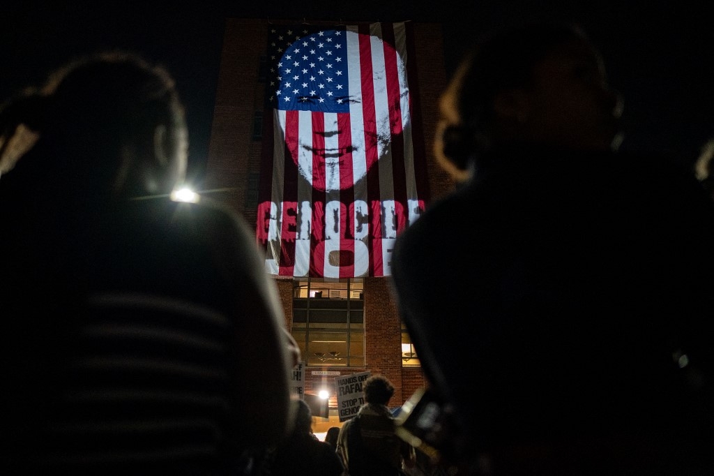 Manifestants pro-palestiniens rassemblés devant projection du visage du président Joe Biden, l’associant au génocide à Gaza, sur un drapeau américain à l'Université George Washington, le 7 mai 2024 à Washington (Kent Nishimura/Getty Images/AFP)