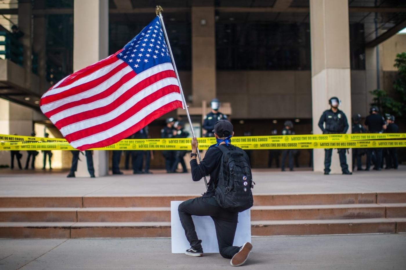 À Anaheim, en Californie, un manifestant tenant un drapeau américain s’agenouille devant des policiers au cours d’une manifestation pacifique suite à la mort de George Floyd, le 1er juin (AFP)
