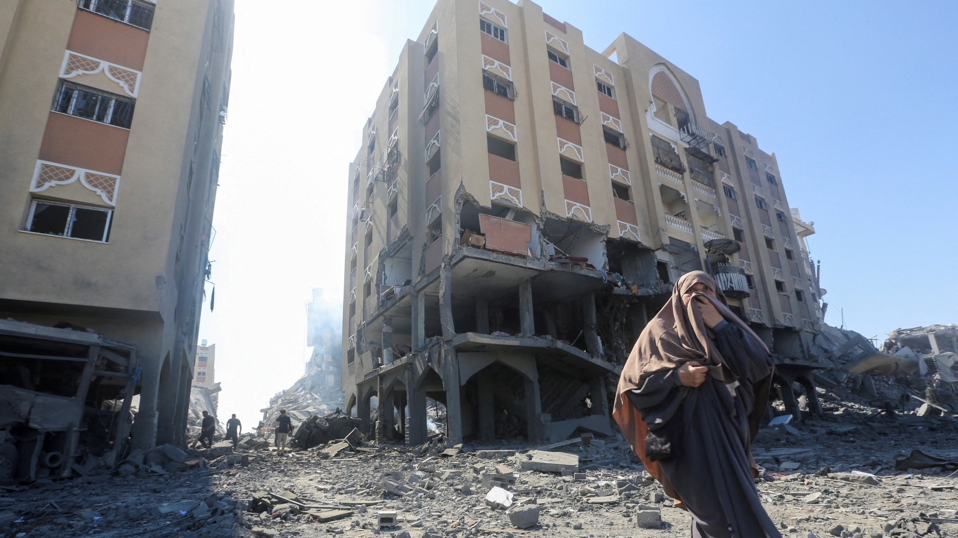 A Palestinian woman walks in front of a damaged residential buildings in Khan Yunis, 13 March (Reuters/Ahmed Zakot)