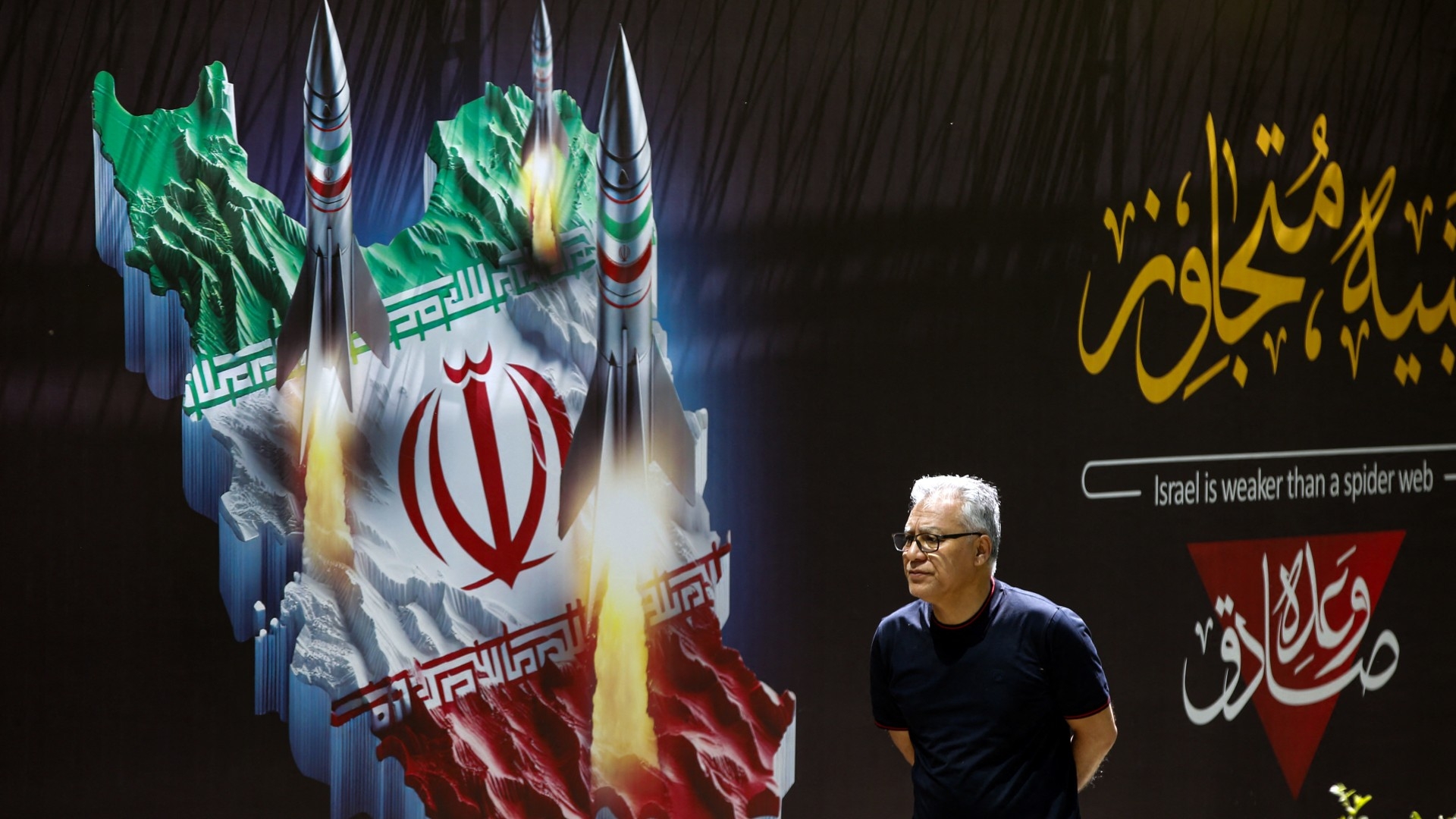 A man walks past a banner depicting missiles along a street in Tehran on 19 April (AFP)