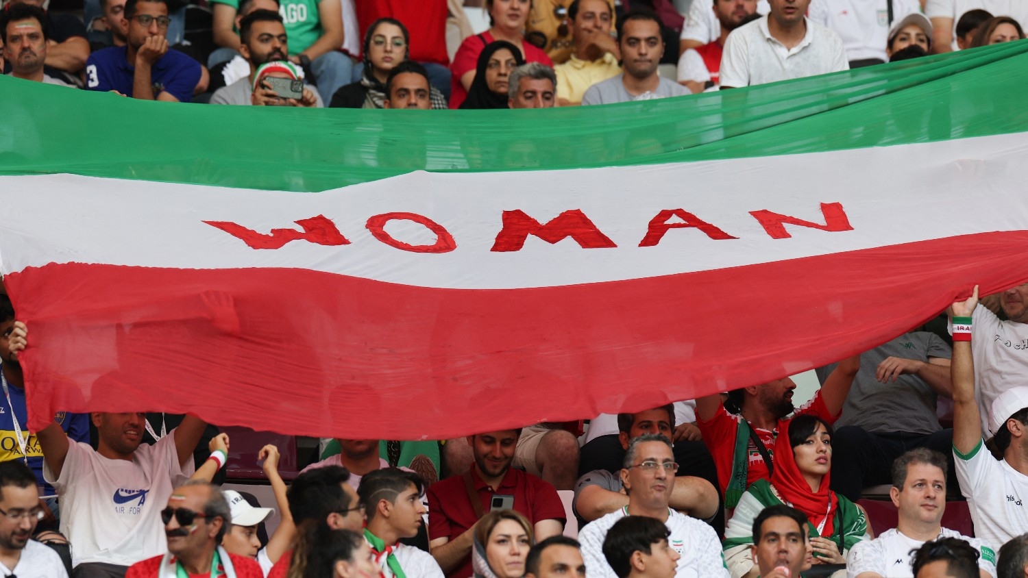 Iran supporters wave their national flag bearing the word "Woman" during the Qatar 2022 World Cup football match between England and Iran in Doha on 21 November 2022.