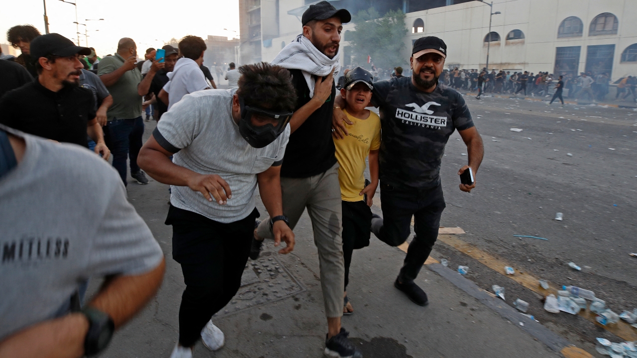 Supporters of Muqtada al-Sadr run for cover from tear gas fired by security forces amid clashes in Baghdad's Tahrir Square on 28 September 2022
