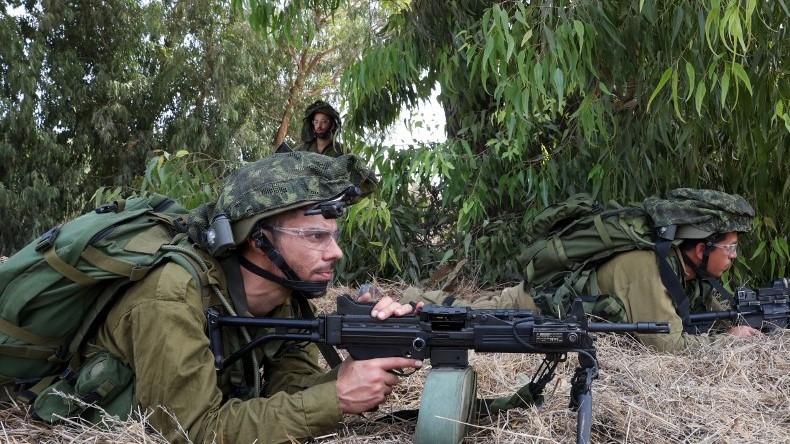Israeli soldiers take up position in Kfar Aza, south of Israel bordering Gaza Strip, on 10 October 2023 (AFP)