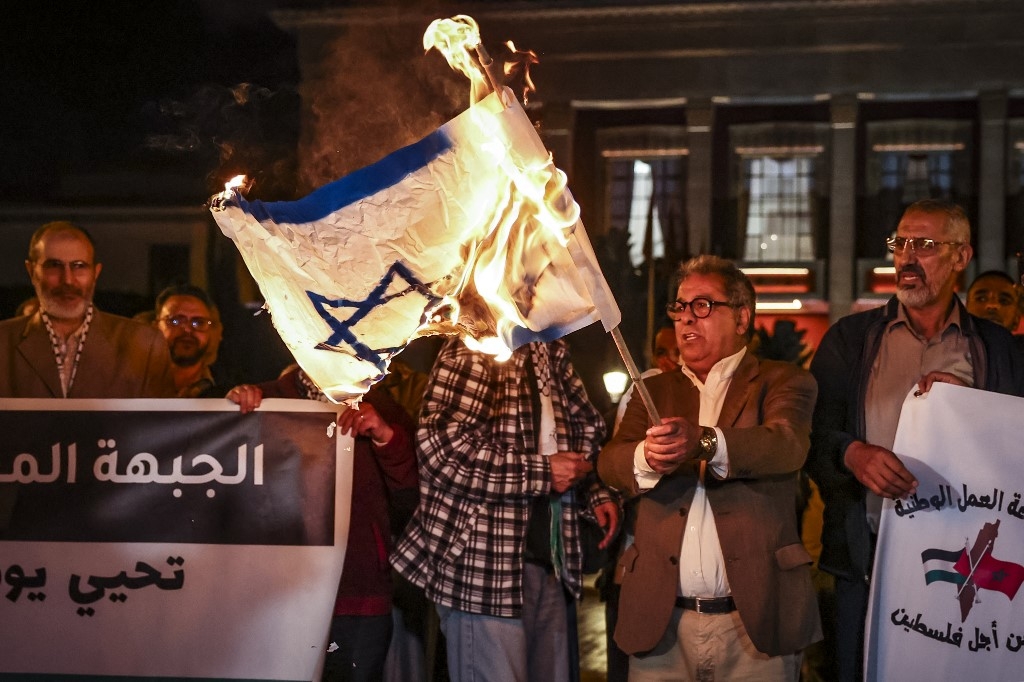 Pendant une manifestation en soutien à la Palestine devant le Parlement de Rabat, un Marocain brandit un drapeau israélien en feu (AFP/Fadel Senna)