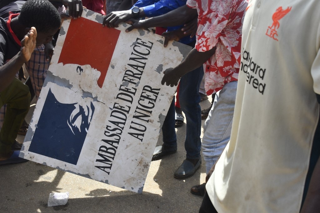 Des manifestants tiennent une pancarte décrochée de l’ambassade de France à Niamey, lors d’une manifestation qui a suivi un rassemblement de soutien aux militaires putschistes, à Niamey, le 30 juillet 2023 (AFP)