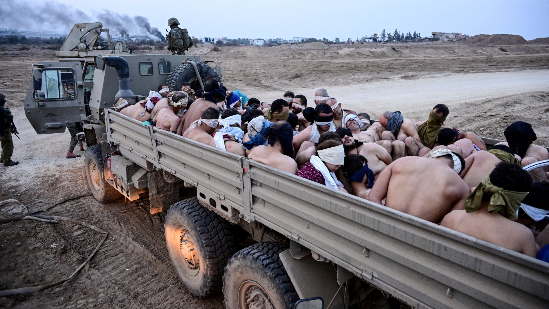 Israeli soldiers stand by a truck packed with shirtless Palestinian men and one woman in the besieged Gaza Strip on 8 December 2023 (Reuters/Yossi Zeliger)