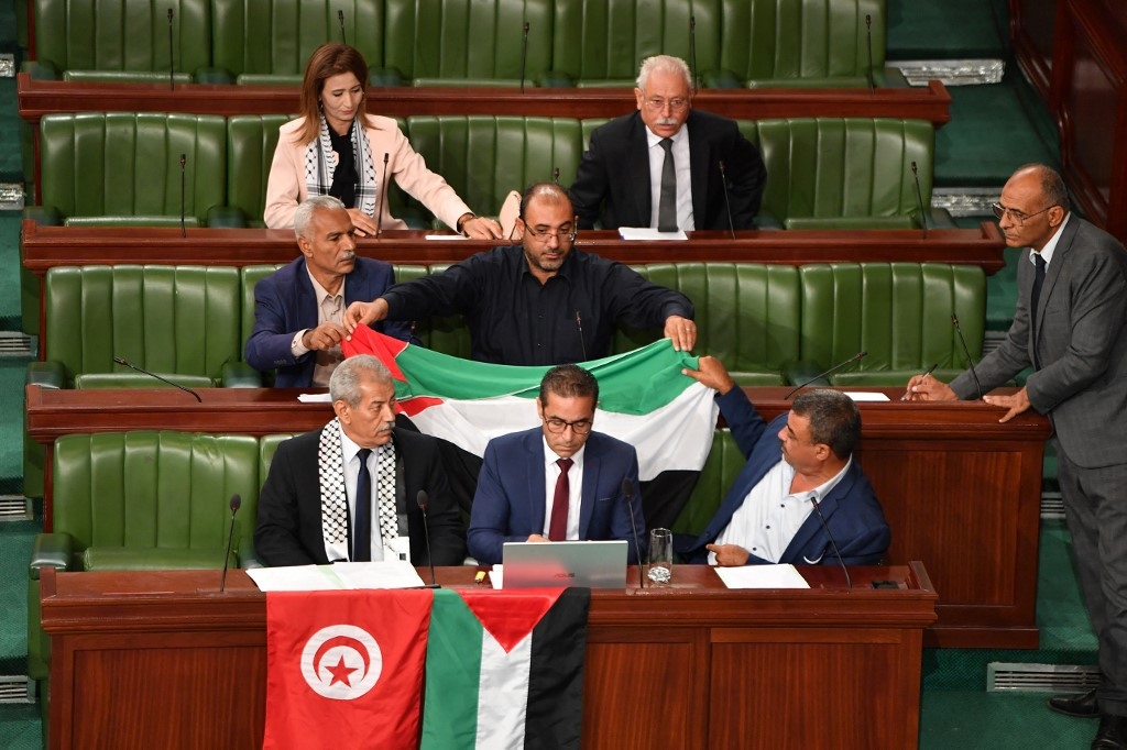 Des parlementaires tunisiens déplient le drapeau palestinien lors d’une minute de silence pour les victimes palestiniennes de Gaza, à l’ouverture d’une séance consacrée à un projet de loi sur la criminalisation de la normalisation avec Israël, le 2 novembre (AFP/Fethi Belaïd)
