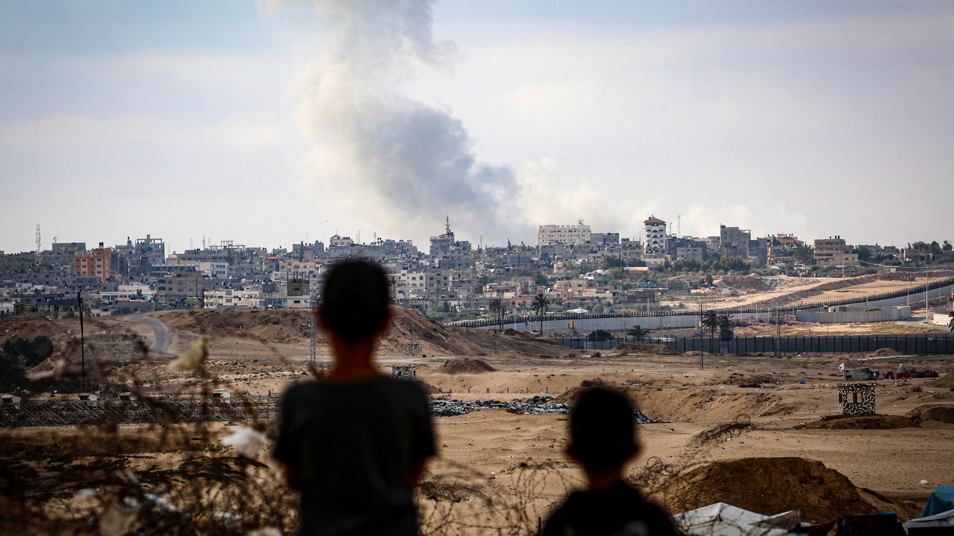 Boys watch smoke billowing during Israeli strikes east of Rafah in the southern Gaza Strip on 13 May 2024 (AFP)