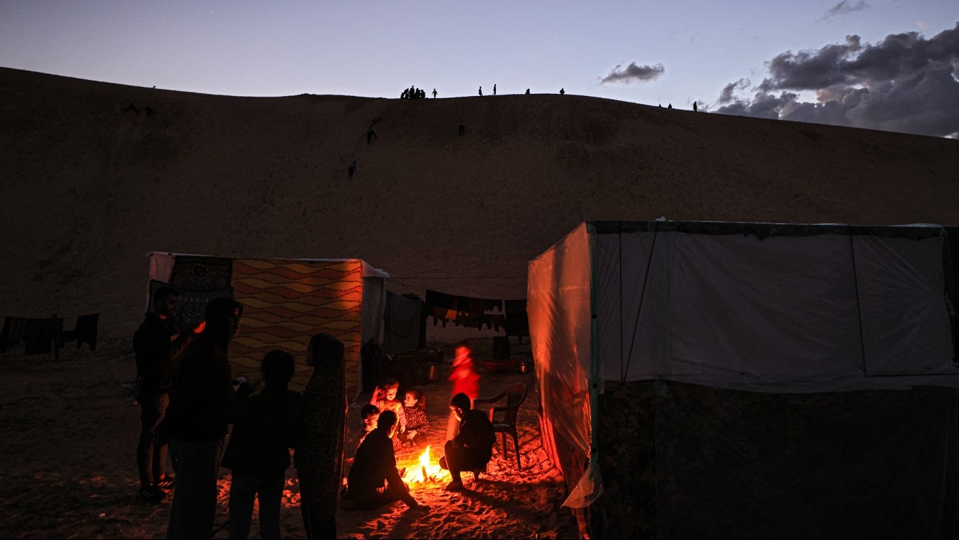 Displaced Palestinians warm themselves by a fire at a makeshift camp west of Rafah near the Egyptian border on 14 January 2024 (AFP)
