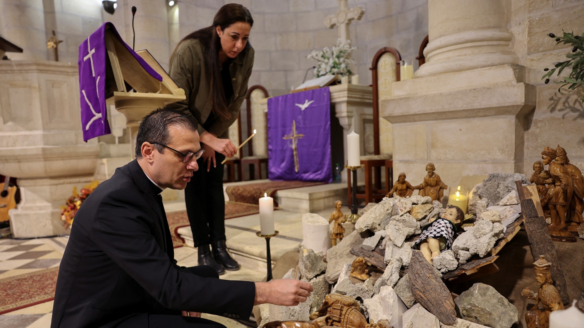Pastor Munther Isaac adds dirt to an installation that shows a figure symbolizing baby Jesus lying amidst the rubble in a grotto ahead of Christmas at the Evangelical Lutheran Church (Reuters)