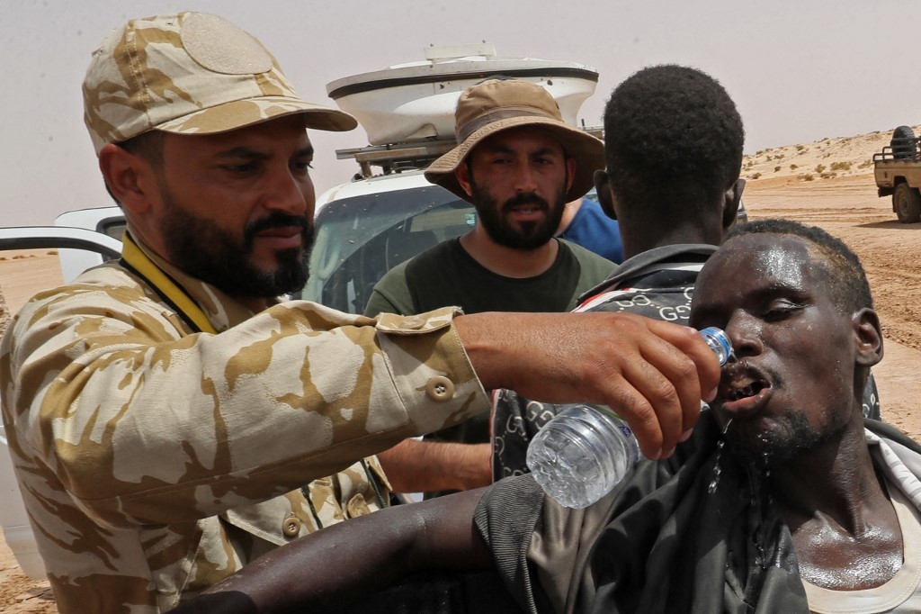 Des gardes-frontières libyens fournissent de l’eau aux migrants d’origine africaine déportés par les autorités tunisiennes à la frontière Libye-Tunisie, le 30 juillet 2023 (AFP/Mahmoud Turkia)