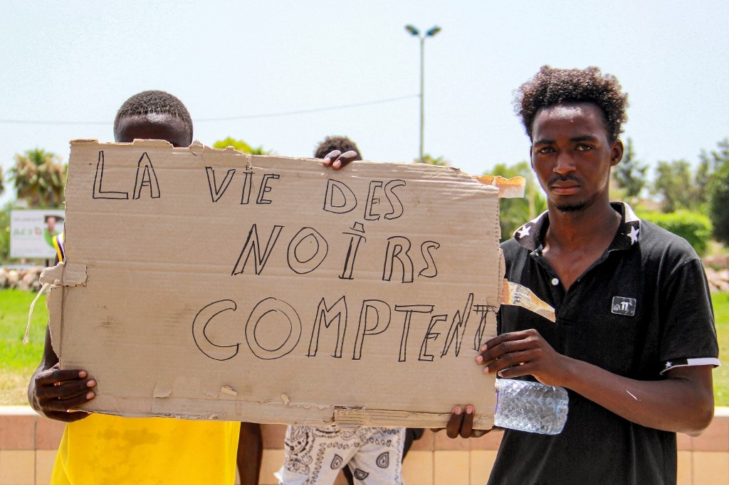 Des migrants subsahariens tiennent une pancarte lors d’une manifestation contre les conditions désastreuses des migrants dans la ville de Sfax en Tunisie, le 7 juillet 2023 (AFP/Houssem Zouari)