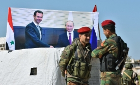 Des soldats syriens discutent à côté des portraits de Vladimir Poutine et Bachar al-Assad, au point de passage d’Abou Douhour, au nord-ouest de la Syrie, le 4 avril 2018 (AFP/George Ourfalian)