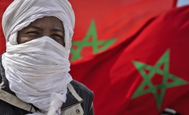 Un membre d’une tribu se tient devant des drapeaux marocains près de la frontière à Guerguerat, le 26 novembre 2020 au Sahara occidental, après l’intervention des Forces armées royales marocaines dans la région (AFP)