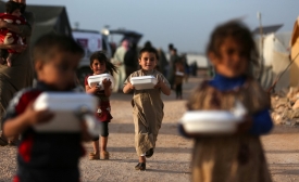 Des enfants syriens déplacés transportent des boîtes de nourriture distribuées par une organisation caritative locale avant l’iftar pendant le mois du Ramadan, dans un camp de déplacés de la province d’Idleb, le 3 avril 2022 (AFP)