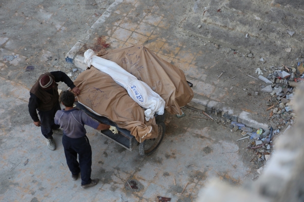 Man carries dead bodies away in Aleppo (MEE/ Zuheir al-Shimale)