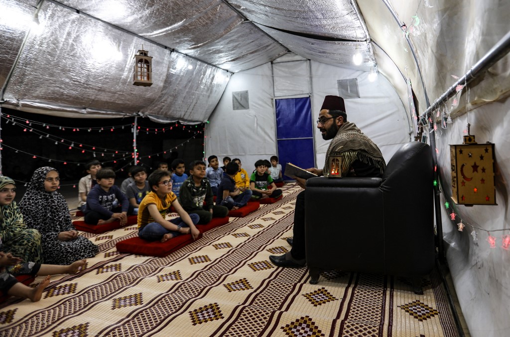 Syrian children listen to a traditional storyteller at a camp for displaced people in northwestern Idlib province on 29 April 2021 (AFP)