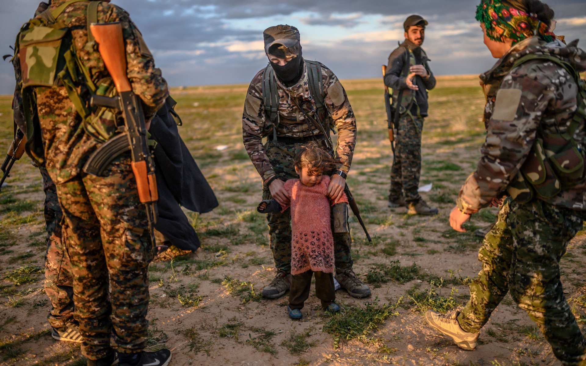 Un membre des FDS tient une enfant en bas âge lors d’un contrôle de sécurité des personnes quittant Baghouz en février 2019 (Bulent Kilic/AFP)