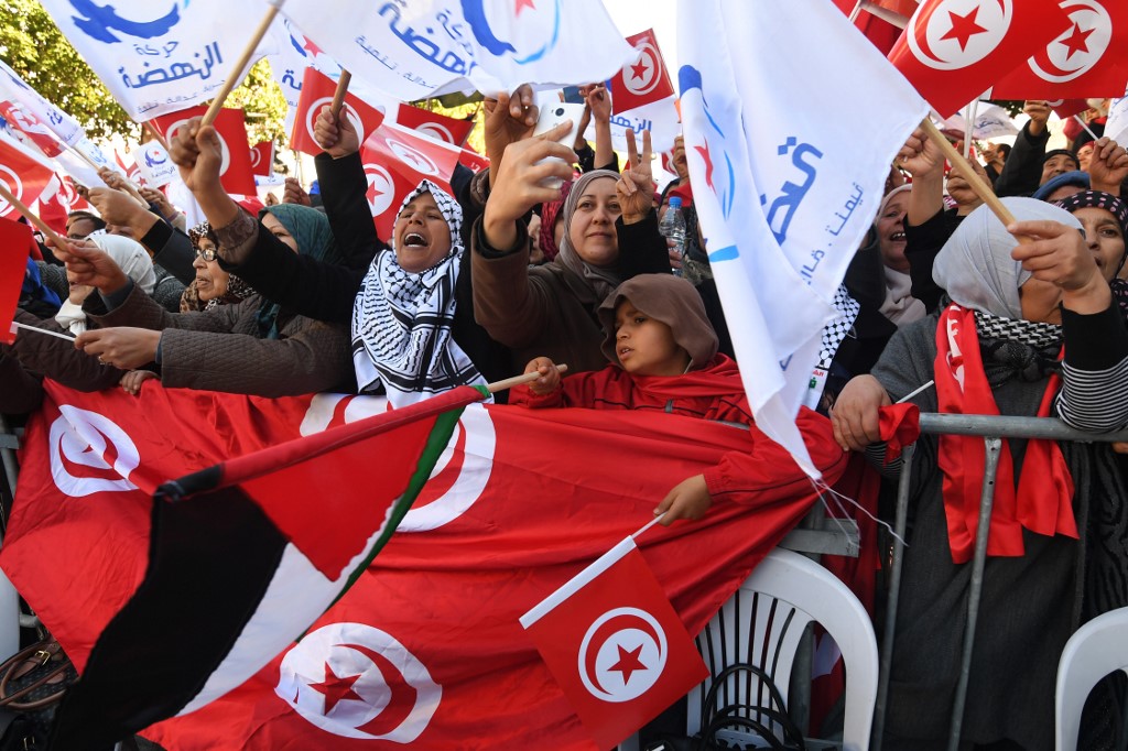 Tunisians wave their national flag and that of Ennahda in Tunis on 14 January 2018 (AFP)