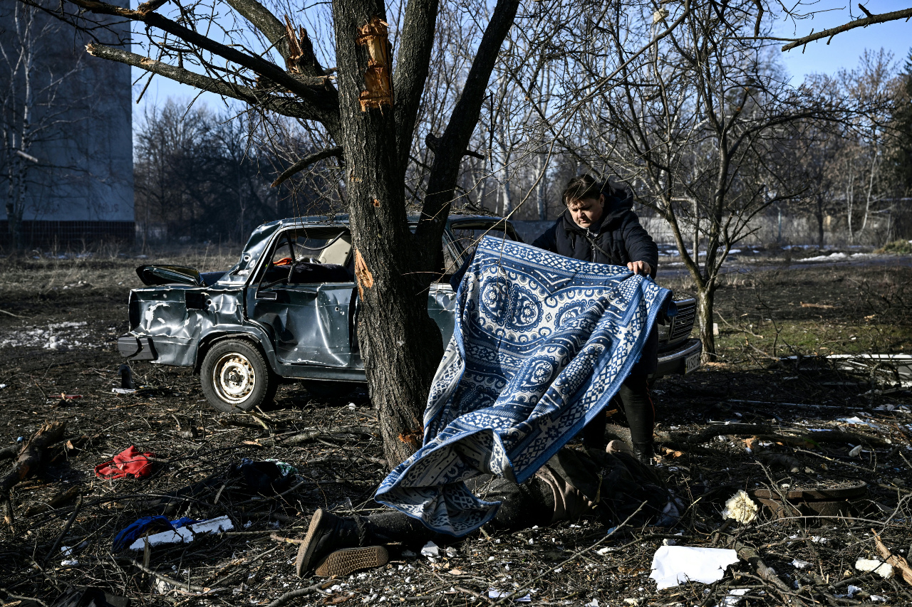A man uses a carpet to cover a body stretched out on the ground after bombings on the eastern Ukraine town of Chuguiv (AFP)